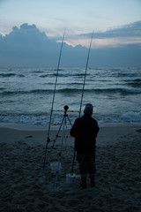 Night fishing, fisherman on the shore with sunset and sea on background, sport, competition on the Baltic Sea, vertical