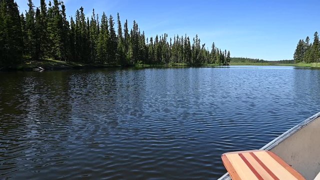Canoe slowly drifting on a river to reveal a scenic view of blue sky above a dark green boreal forest and water with small ripples.  Water drips off a paddle on the side of the canoe.