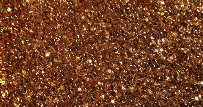Top down view. Gold sequins scattered on the surface shimmer and sparkle. From a sudden blowing, they fly in different directions.