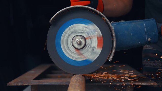 Angle grinder cutting through rusty iron pipe, close up, sparkles
