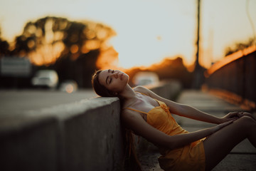 A woman sits on the sidewalk in a yellow dress at sunset.