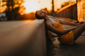 A woman sits on the sidewalk in a yellow dress at sunset.