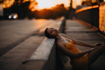 A woman sits on the sidewalk in a yellow dress at sunset.