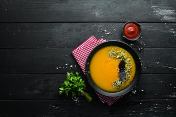 Pumpkin soup with pumpkin seeds in a black plate on a black background. Top view. Free space for your text.