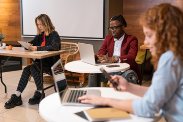 Group of multicultural students using mobile gadgets while preparing homework