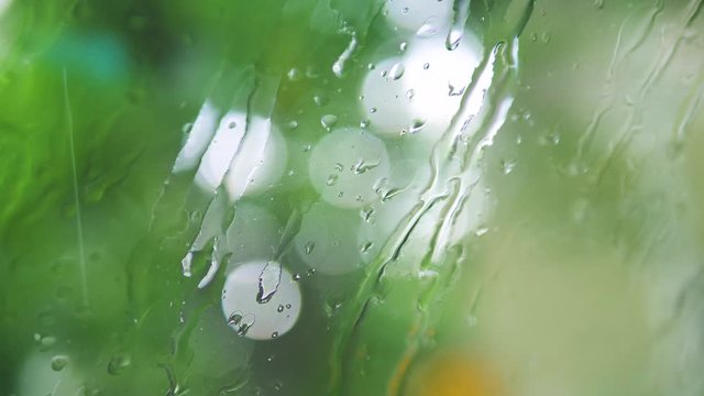 Light rain dripping on a glass, close up, blurry natural background