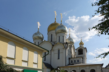 Fototapeta na wymiar Golden domes with crosses of an orthodox temple on the background of bright blue sky. Snow-white facade. Christian faith.
