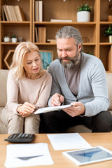 Mature woman listening to her husband pointing at document while reading it