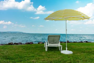 Stylish lounger plastic sunbed with yellow stripes sunshade beach umbrella on the green grass on beach at summer under open sky. Sunbed intended for cold shadow on convenient lounger at Lake Balaton