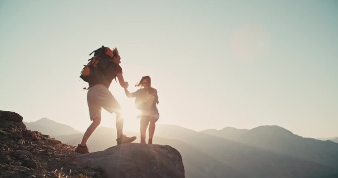Caucasian couple hiking together with backpacks, helping each other on their way up the mountains - freedom, active lifestyle concept 4k footage