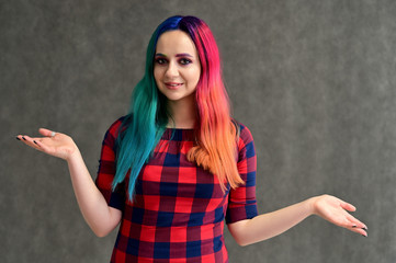 Portrait of a pretty girl with multi-colored hair and makeup on a gray background. Stands with a smile in various poses in the studio.