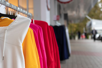 A hanger with brightly colored women's sweaters put up for sale on the street in front of the store...