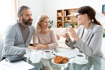 Mature man and woman looking at young consultant while discussing terms of deal