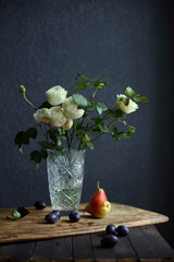still life with white roses and fruit on a dark background. © oksnemova