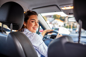 Rear view of attractive young woman in casual wear looking over her shoulder while driving a car....