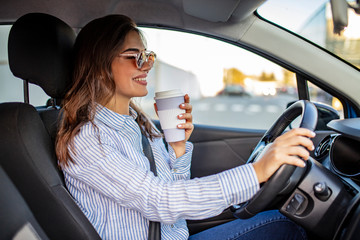 Happy young woman with coffee to go driving her car. Woman sipping a coffee while driving a car. Young woman drinking coffee while driving her car. Attractive brunette drives a car