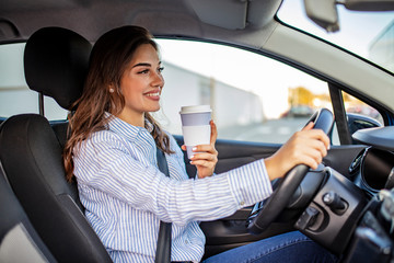 Fototapeta na wymiar Happy young woman with coffee to go driving her car. Side view of woman driving car with coffee to go in hand. Young woman drinking coffee while driving her car