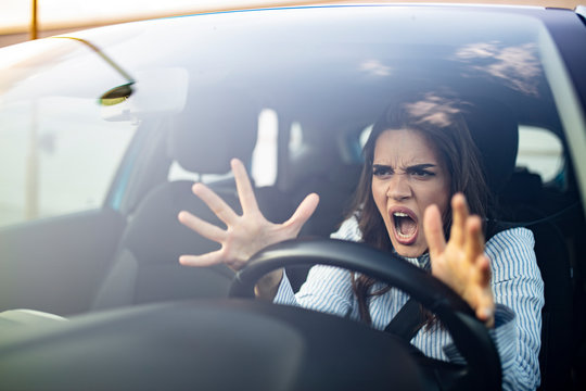 Stressed woman driver sitting inside her car. Angry female driver driving a car. Angry young woman stuck in a traffic jam. Woman annoyed in car. Girl stuck in traffic.