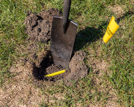 Buried plastic natural gas line in hole of yard. Shovel in soil and yellow buried gas warning flag marking location. Concept of notify utility location company for underground utitilies before digging