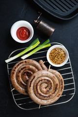 Barbecued rolled sausages on a metal cooling rack, view from above on a black stone background