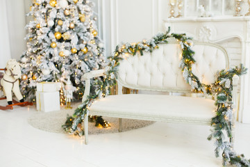Stylish romantic Christmas light interior with a soft armchair or sofa decorated with garland from artificial spruce twigs. Comfort home. Christmas tree with presents underneath in living room