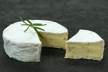  Camembert cheese with herbs decorated with a sprig of rosemary on a black background. Copy space.