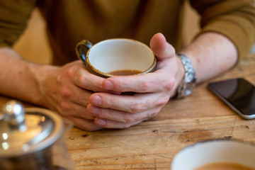 Fototapeta na wymiar Male hands round coffee cup at wooden cafe table