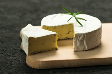 Camembert cheese with greens decorated with a sprig of rosemary on a wooden board on a black...