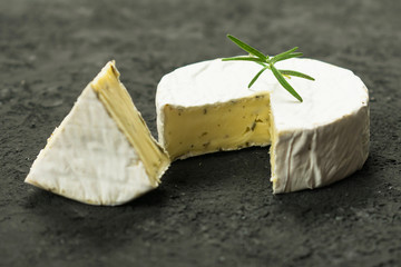 Camembert cheese with a sprig of rosemary  on a black background.