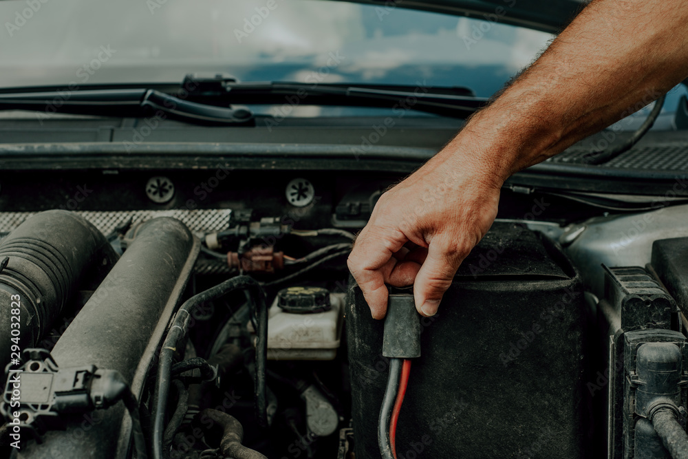Poster checking the battery in the car. concept of car failure, problems with firing a car. the man checks 