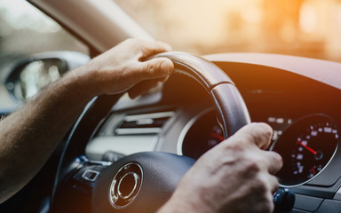 The man is holding his hands on the steering wheel of the car. The concept of driving a car. The interior of a modern car. View of the steering wheel, the dashboard of the car.