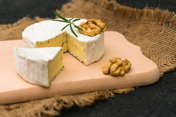 Camembert cheese with greens garnished with a sprig of rosemary and walnut on a wooden board.