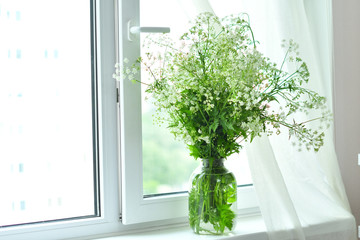 Bouquet of white wildflowers in a basket on window. Rustic still life. Coziness in the house
