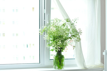 Bouquet of white wildflowers in a basket on window. Rustic still life. Coziness in the house