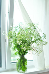 Bouquet of white wildflowers in a basket on window. Rustic still life. Coziness in the house