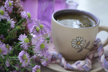 Morning hot coffe in mug and little violet flowers. Blurred background.