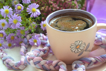 cup of coffee next to autumn purple flowers on wooden texture.