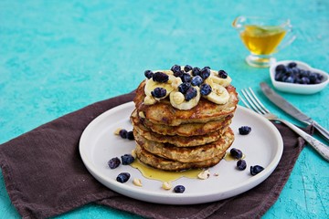 Banana oat pancakes with hazelnuts, sliced banana, honey and honeysuckle on a white plate on a...