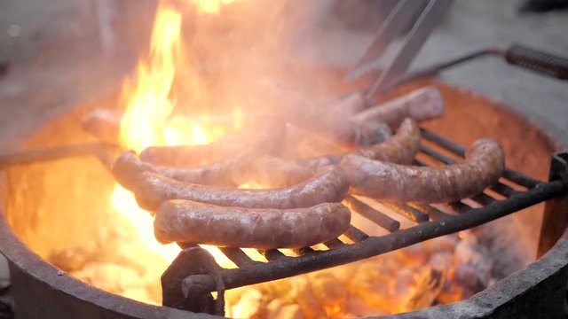 Slow motion grilling kielbasa sausage over a campfire of glowing coals.