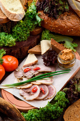 Meat beer snack. Fresh slices of delicious bacon, horseradish and croutons of dark and light bread on a light wooden board on a dark wooden background among fresh vegetables. Close-up