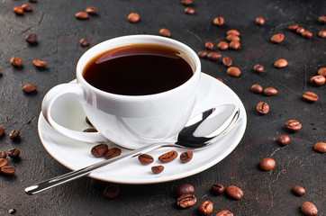 A Cup of coffee on a saucer and coffee beans on a dark background.