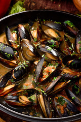 Mussel shells in cream sauce in a black cauldron on a dark wooden background, decorated with vegetables. Close-up. Space. Photo series