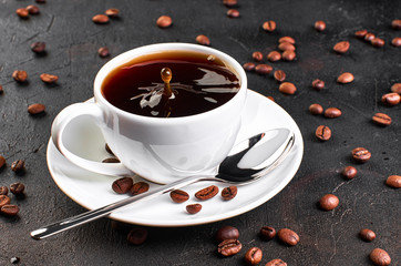 A Cup of coffee on a saucer and coffee beans on a dark background. A drop of coffee splashed in the Cup.