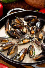 Mussel shells in cream sauce in a black cauldron on a dark wooden background, decorated with vegetables. Close-up. Space. Photo series
