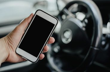 A telephone with a blank display on the background of the steering wheel and dashboard. The man is...