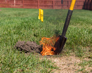 Real black smoke and flames rise from fire in hole of yard. Natural gas warning flag and shovel....