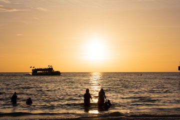 Sun backlights a ship or boat in the back while people get to shore to dry off with a towel