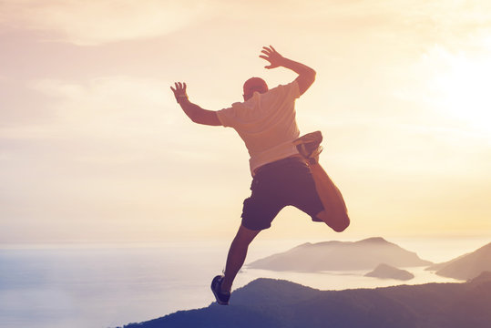 Young man hovered in a jump in the air against the seascape and mountains at sunset, rear view, toned. Concept of freedom, happiness, success.