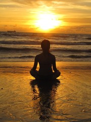 Young woman sitting on the beach, silhouette at sunset. Young woman practicing yoga outdoors. Harmony and meditation concept. Healthy lifestyle. meditate in lotus yoga