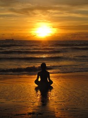 Young woman sitting on the beach, silhouette at sunset. Young woman practicing yoga outdoors. Harmony and meditation concept. Healthy lifestyle. meditate in lotus yoga